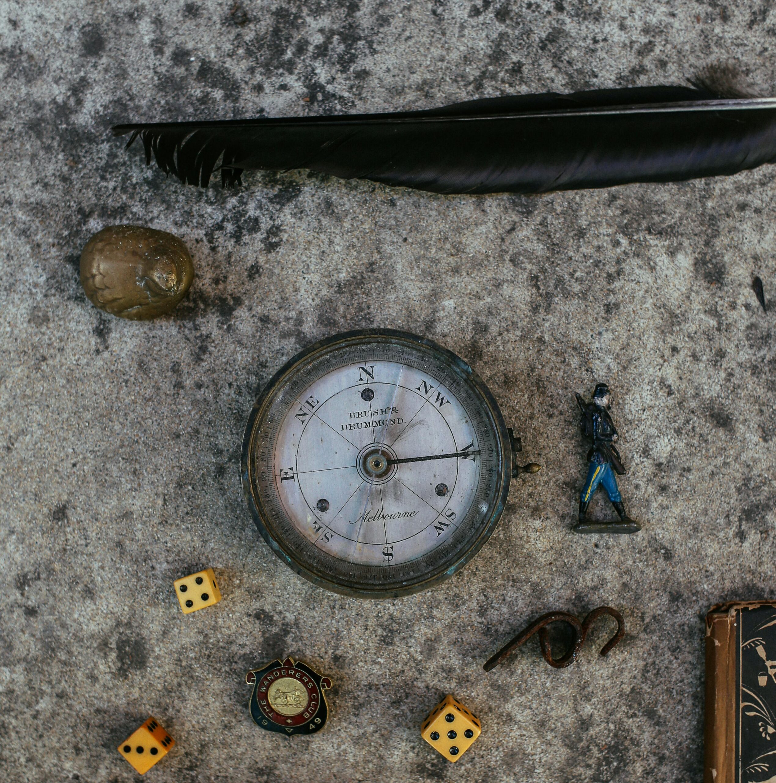 Top view of vintage items including compass, feather, and dice on stone surface.